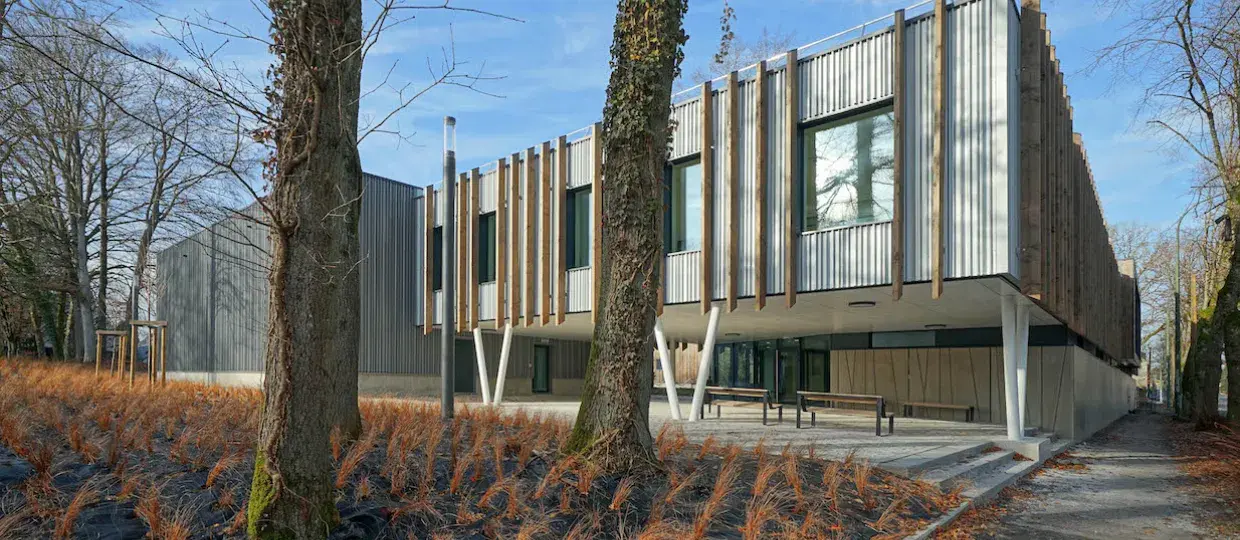 The Durabilis office building in Arlon: a two-storey building with corrugated metal and vertical timber cladding, set among mature trees.